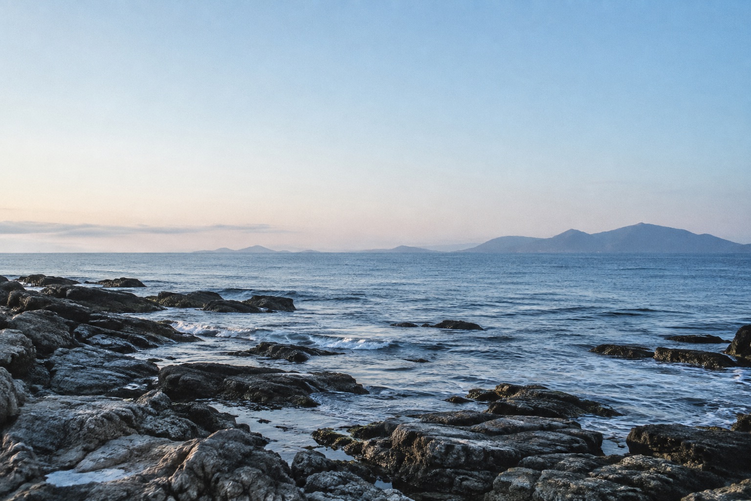 青い海と山の稜線が静かに重なる、夜明けの海辺